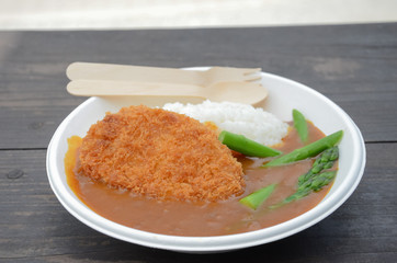 Curry rice with fried pork and asparagus on white plate on wood table