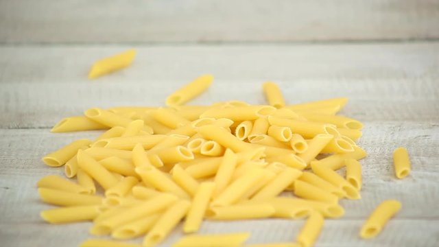 Hands pouring Penne pasta onto wood in slow motion