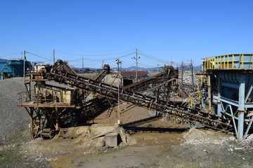 Fototapeta premium 砕石場／山形県の庄内地方で、建設資材用の砂利や砂を生産する、砕石場を撮影した写真です。砕石した砂や砂利を長いコンベアで搬送し、真下に落とす機械設備が設置された建設資材現場の風景です。