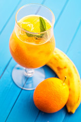 fresh orange smoothie with mint leaf in glass on blue wooden background, orange, mango, carrot or banana drink, product photography for healthy lifestyle