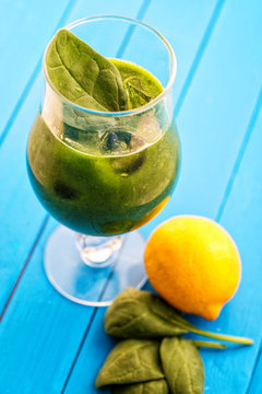 fresh green smoothie with spinach leaf and lemon in glass isolated on blue background, spinach, cucumber, apple fruit drink, product photography for healthy lifestyle
