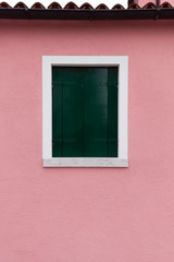 Window with dark green shutters on light pink wall