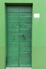 Old wooden green locked door with peeling paint in the green wal