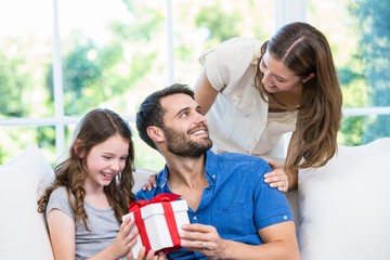 Man looking at wife while holding gift with daughter 