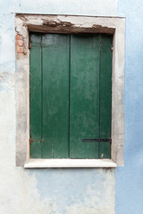 Fototapeta na wymiar Old window with dark green shutters on light blue wall