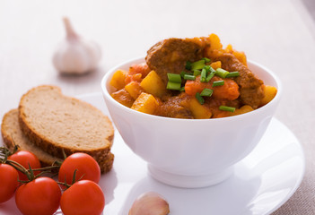 Homemade goulash with slices of bread in white bowl
