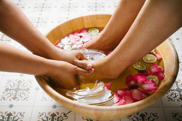 Obraz na płótnie Canvas Closeup shot of a woman feet dipped in water with petals in a wooden bowl. Beautiful female feet at spa salon on pedicure procedure. Shallow depth of field with focus on feet. 