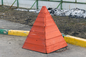 Wooden safety cone stands on a sewer manhole