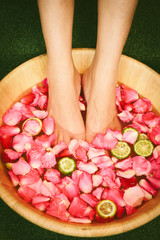 Closeup shot of a woman feet dipped in water with petals in a wooden bowl. Beautiful female feet at...