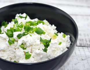 Cottage cheese with chives in black ceramic bowl 