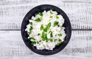 Cottage cheese with chives in black ceramic bowl 