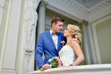 Wedding couple indoors is hugging each other. Beautiful model girl in white dress. Man in suit. Beauty bride with groom. Female and male portrait. Woman with lace veil. Cute lady and handsome guy