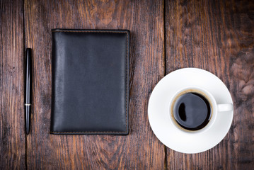 Fototapeta na wymiar a leather notebook, a pen and cup of coffee on a wooden background
