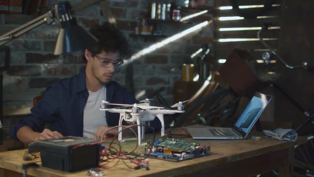 Man is soldering electrical components on a drone in a garage while checking a laptop computer. Shot on RED Cinema Camera.
