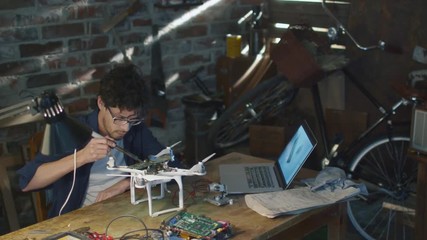 Student is soldering electrical components on a drone in a garage while checking a laptop computer. Shot on RED Cinema Camera.