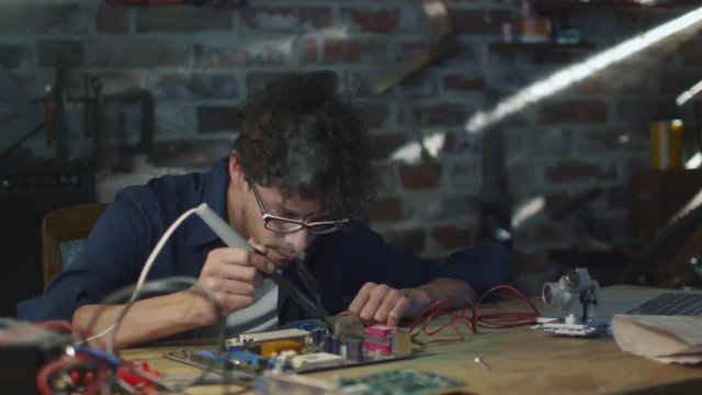 Student is studying electronics and soldering a circuit board in a garage. Shot on RED Cinema Camera.