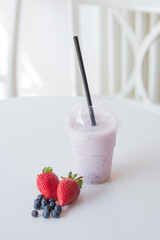 smoothie in plastic cup at the table with strawberry and blackbe