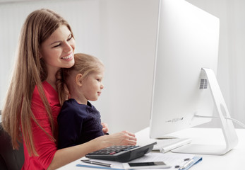 Young joyful mother calculating family budget sitting with her daughter at the desk. Concept of investment and banking. 