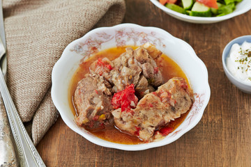Meat stew in spicy tomato sauce on a wooden table.