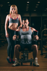 Fototapeta na wymiar beautiful young sporty sexy couple showing muscle and workout in gym dumbbell