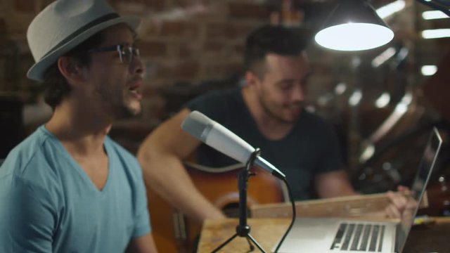Two young man sing and play guitar while recording a song in a home studio in a garage. Shot on RED Cinema Camera.