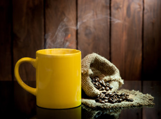Yellow coffee cup and coffee beans on old wooden background.