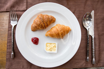 Two croissants on a white plate close up, view from above, wooden background