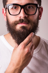 Obraz premium Face portrait of bearded man in glasses with hand on beard against white background