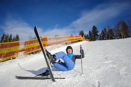 Young female skier in blue ski suit after the fall on mountain slope against ski lift and winter mountains background. Ski resort. Winter sports concept.