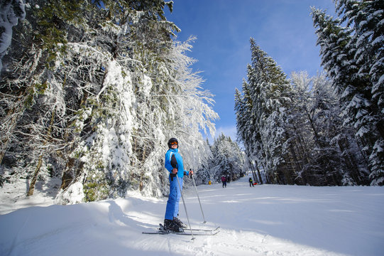 Full length portrait of happy skier on a ski slope in the forest with big beautiful trees covered in snow. Winter sports concept. Bukovel, Ukraine