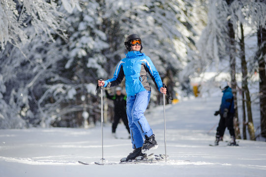 Portrait of young female skier is putting on her skis and looking to the sun on a sunny day against beautiful snow covered trees on the background. Ski resort. Carpathian Mountains, Bukovel