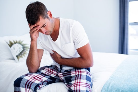 Young man sitting with stomach pain on bed