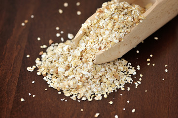 Oat flakes in wooden scoop on wooden background