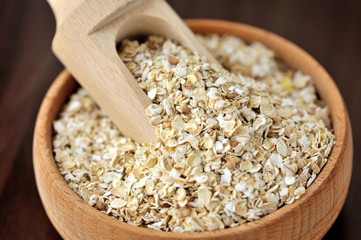 Oatmeal or oat flakes in bowl and scoop on dark wooden table