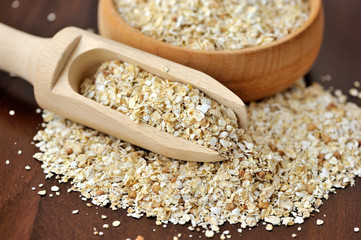 Oatmeal or oat flakes in bowl and scoop on dark wooden table