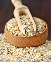 Oatmeal or oat flakes in bowl and scoop on dark wooden table