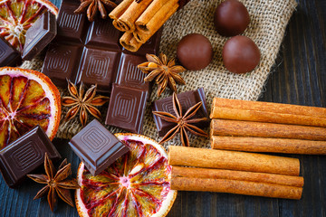 Dark and milk chocolates with dry oranges, candies, cinnamon and anise on burlap on rustic wooden...