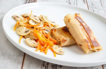 Roasted mushrooms with onion, carrot and two pancake filled with cheese on white cookware