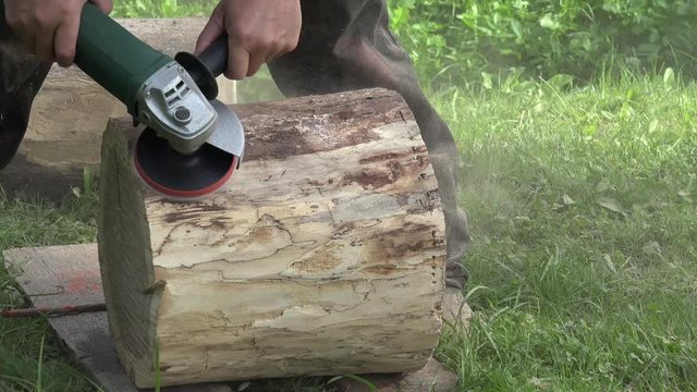 Worker man hand with electric sander tool sand tree log. Carpenter man making decorative chair. Dust rising in air. Static closeup shot. 4K
