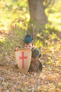 Cute little knight playing with a sword and a shield hiding in the forest
