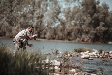 Fly fisherman using fly fishing rod on mountain lake.