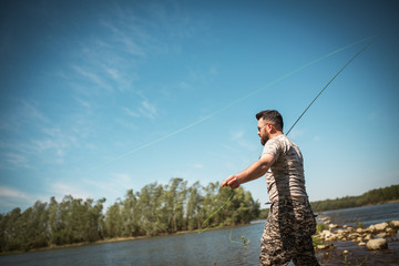 Fly fisherman using fly fishing rod on mountain lake.