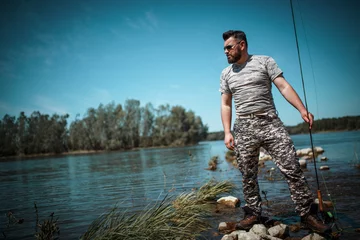 Fotobehang Fly fisherman in camouflage standing next to the river. © BalanceFormCreative