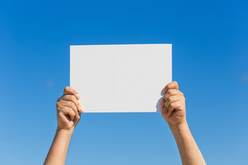 Blank white board in hands against blue sky background