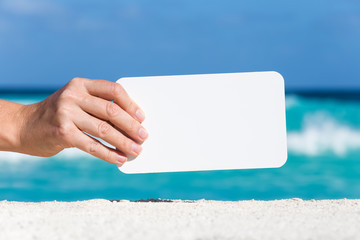 Blank white board in female hand on sand against turquoise carib