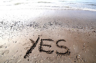 writing on the sand of the sea with the word YES