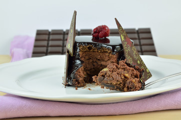 Chocolate cake on white porcelain plate with one bite in spoon and bars of dark chocolate behind