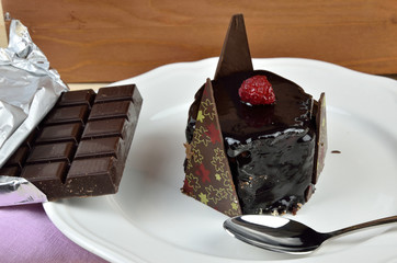 Delicious chocolate cake on white porcelain plate with one bite in spoon and bars of just opened chocolate beside