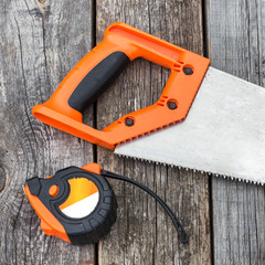 Handsaw and  measuring tape on a wooden board