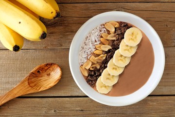 Peanut-butter banana, chocolate smoothie bowl scene on rustic wood background